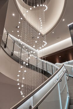 A sweeping 30-foot staircase above the lobby bar is punctuated by a dramatic spiraling custom chandelier by Sapphire Manufacturing made of acrylic faceted beads, powder-coated steel top housing, aircraft cables, LED can lights, and LED globe lights.