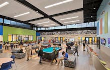 A large, open game room space anchors the project at the center, surrounded by programmed spaces along the perimeter such as classrooms, a teen lounge, a community room, a gymnasium, performing arts center and an administration wing.