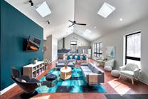 The design turned a formerly dark, dingy living room into a large, open, light-filled space thanks to the expansive windows and skylights, with rich, deep teal accents that extend from the great room to the kitchen beyond.