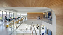 Interior view from top of staircase in two-story Inova Health Center featuring a curved, wood wall, seating areas next to large daylit windows and people interacting in the space. Interior view from top of staircase in two-story Inova Health Center featuring a curved, wood wall, seating areas next to large daylit windows and people interacting in the space.