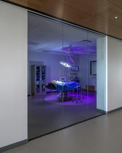 View of surgery classroom through glass door with operating table cast in purple light. View of surgery classroom through glass door with operating table cast in purple light.