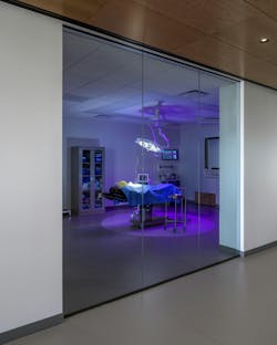 View of surgery classroom through glass door with operating table cast in purple light. View of surgery classroom through glass door with operating table cast in purple light.