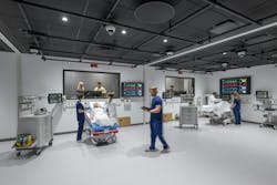 Large, open surgical classroom with two hospital beds with patients and medical machinery with student doctors attending. Large, open surgical classroom with two hospital beds with patients and medical machinery with student doctors attending.