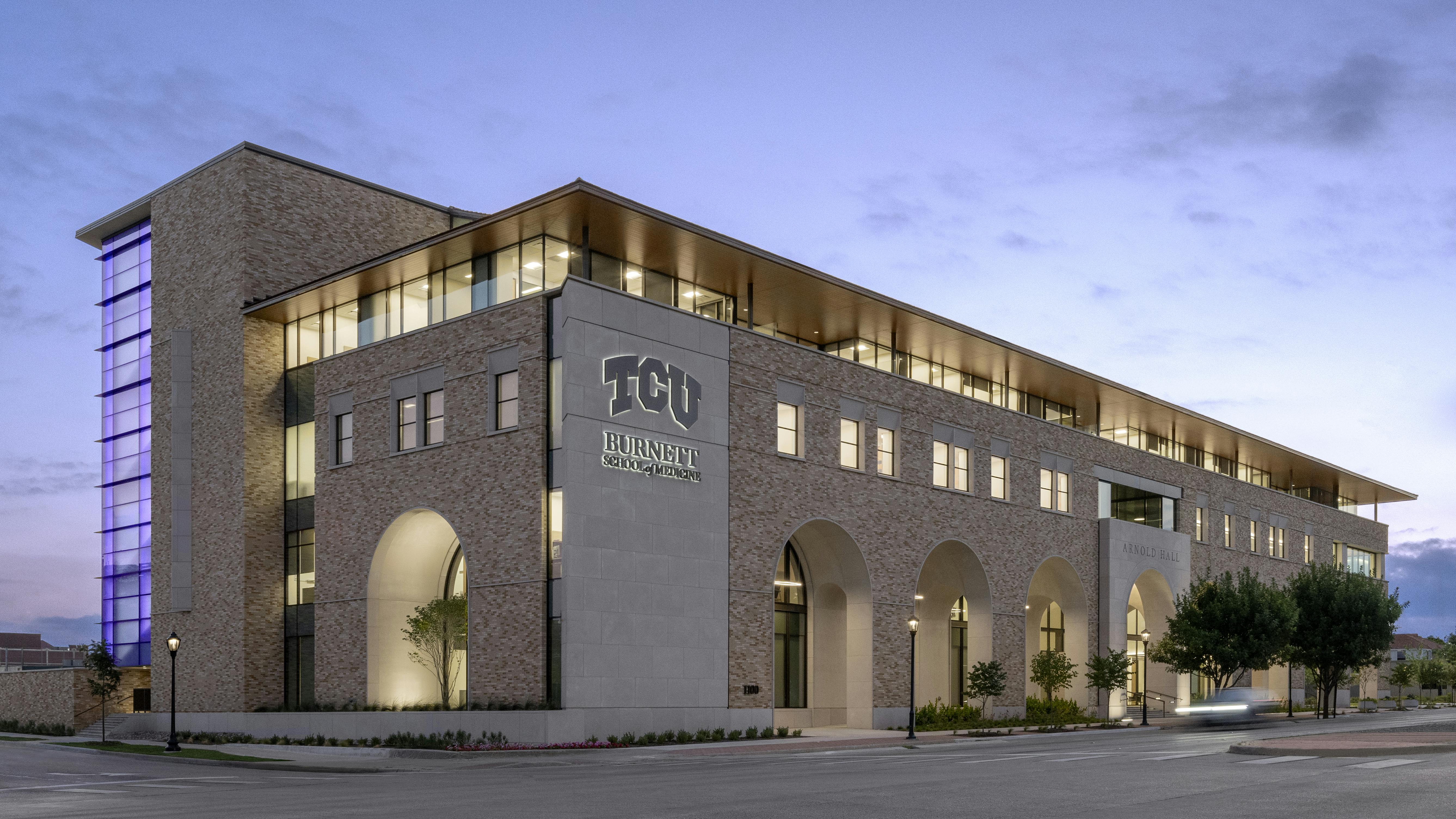 Exterior view of four-story TCU medical school building at dusk.