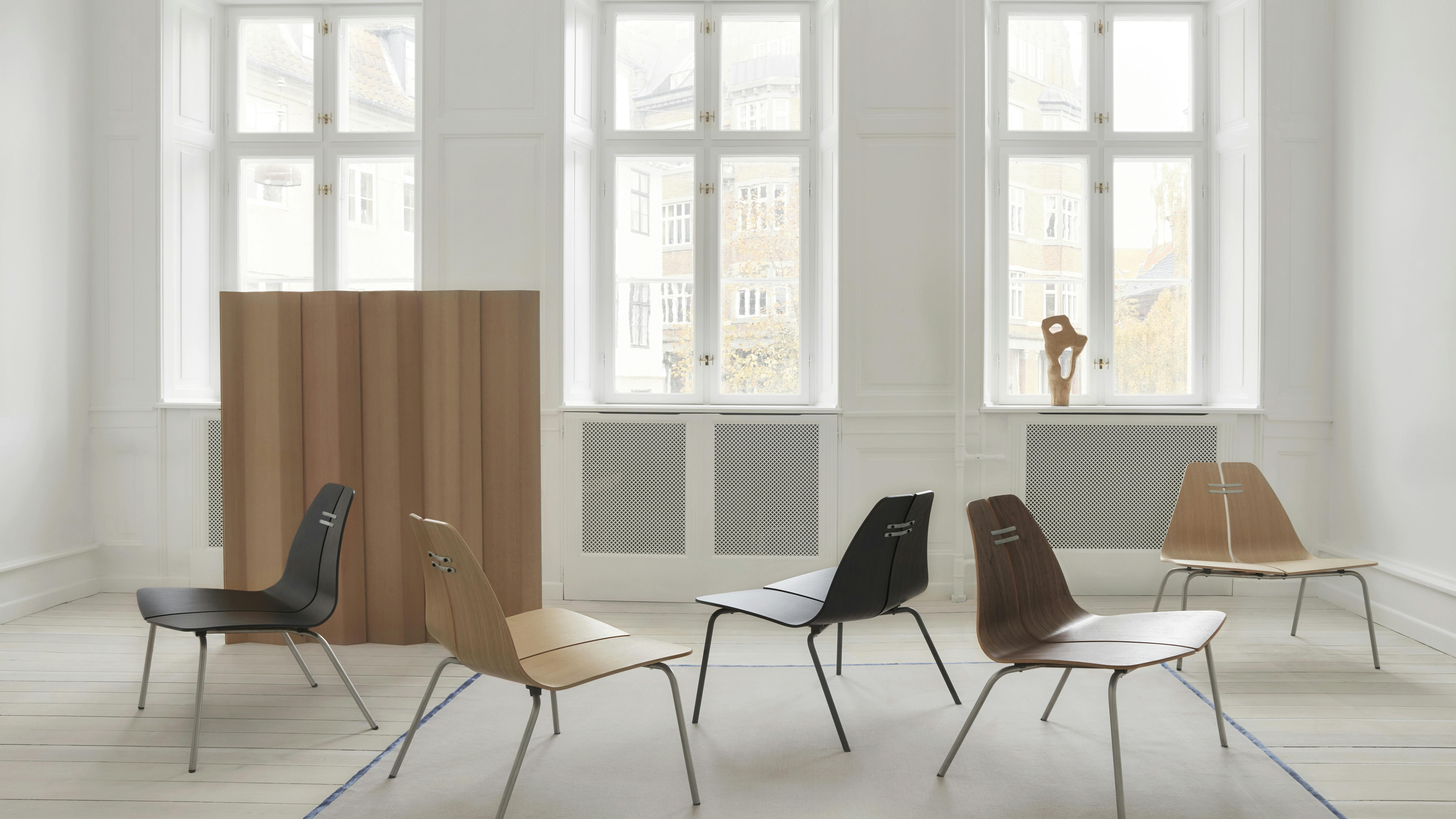 The PK23 chair features wide, low-profile laminated veneer shells for the seat and back. Five chairs are staggered in a room.