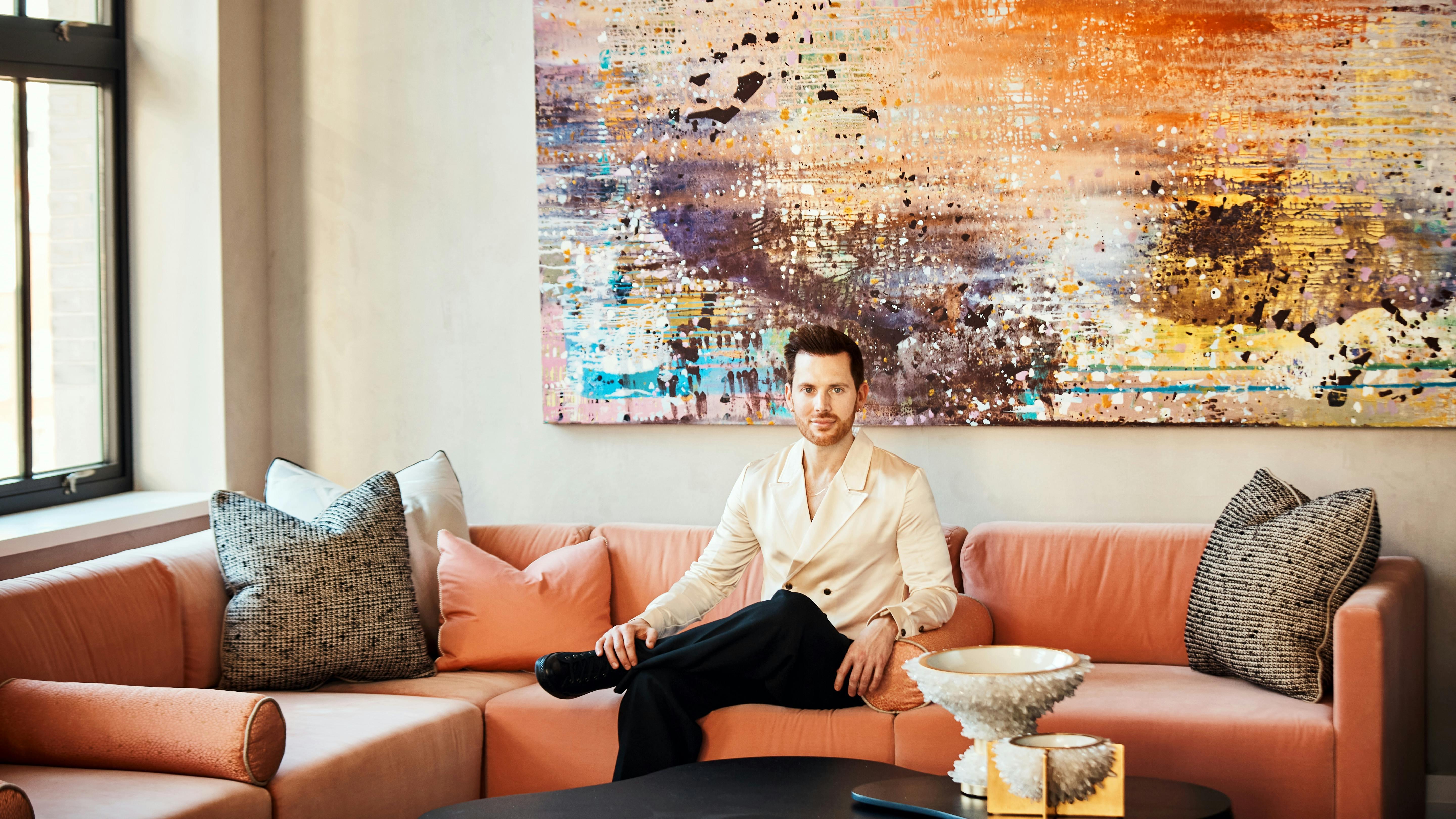 Caleb Anderson, Drake/Anderson Principal, on a deep orange sectional sofa with an abstract artwork in background