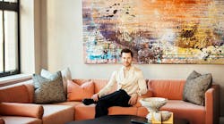 Caleb Anderson, Drake/Anderson Principal, on a deep orange sectional sofa with an abstract artwork in background Caleb Anderson, Drake/Anderson Principal, on a deep orange sectional sofa with an abstract artwork in background