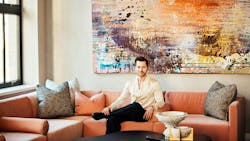Caleb Anderson, Drake/Anderson Principal, on a deep orange sectional sofa with an abstract artwork in background Caleb Anderson, Drake/Anderson Principal, on a deep orange sectional sofa with an abstract artwork in background