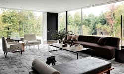 A modern sitting room with expansive window views to the surrounding treeline, with foliage changing in the fall A modern sitting room with expansive window views to the surrounding treeline, with foliage changing in the fall