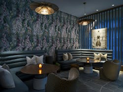 A moody lounge area with graphic printed wallpaper behind booth seating inspired by NYC social lounges. A moody lounge area with graphic printed wallpaper behind booth seating inspired by NYC social lounges.