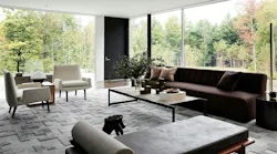 A modern sitting room with expansive window views to the surrounding treeline, with foliage changing in the fall