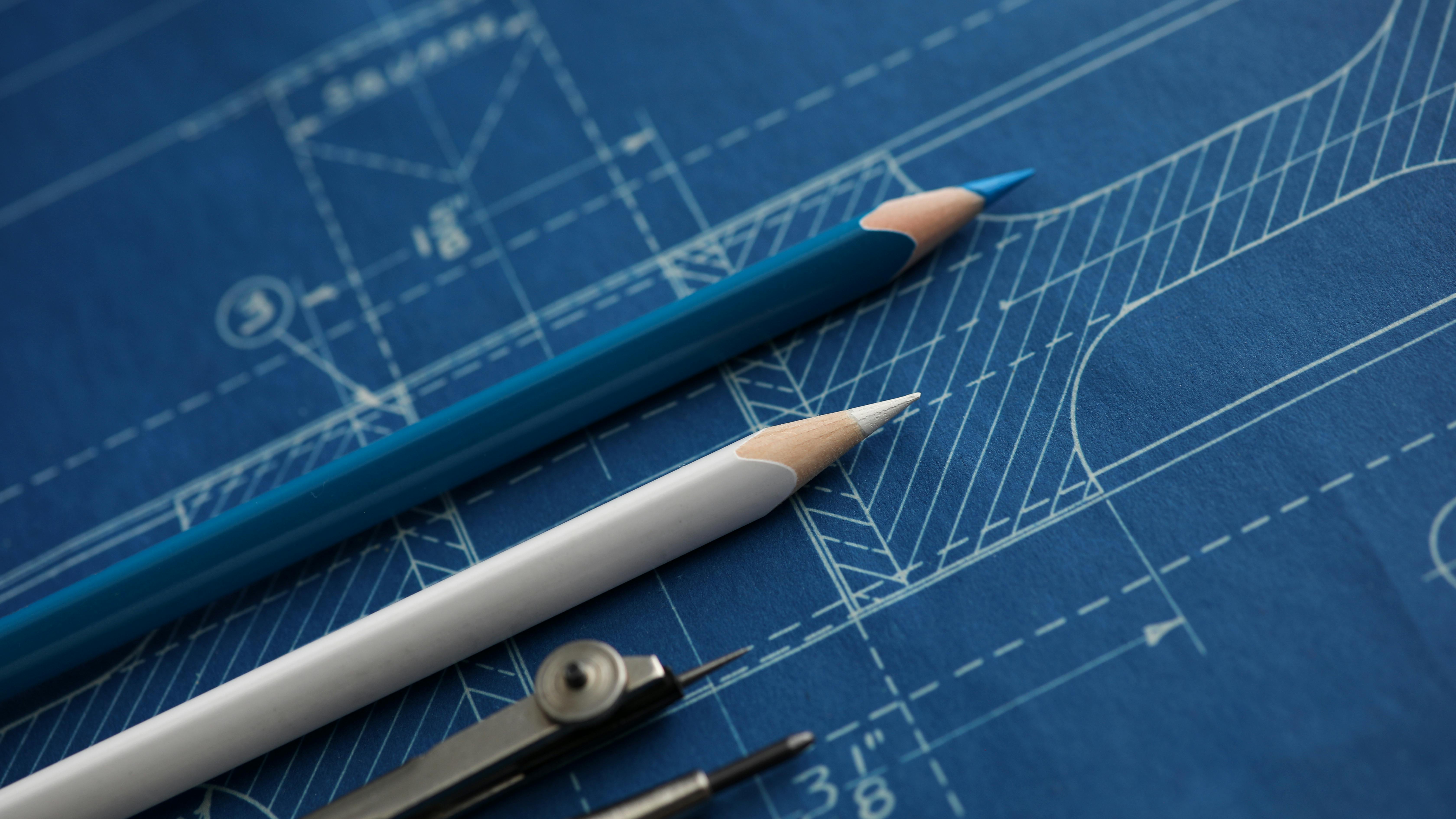 Close up of colored pencils and a protractor on top of a building blueprint.
