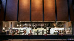 Amelia Gene's open kitchen with large, industrial looking cooper hood faces the main restaurant seating Amelia Gene's open kitchen with large, industrial looking cooper hood faces the main restaurant seating