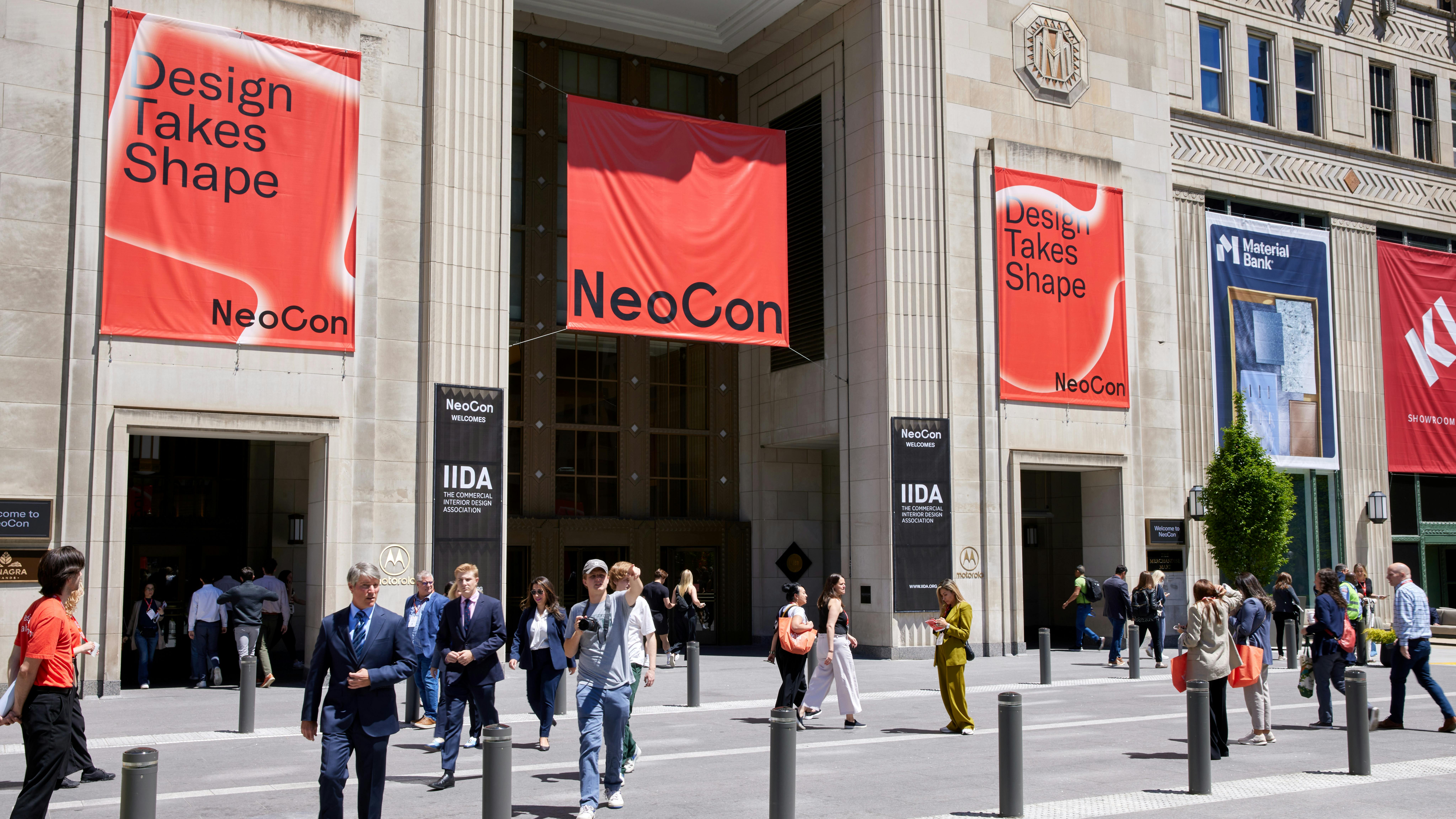 Exterior view of entrance to The MART in Chicago with NeoCon signage and people walking in front of building plaza.
