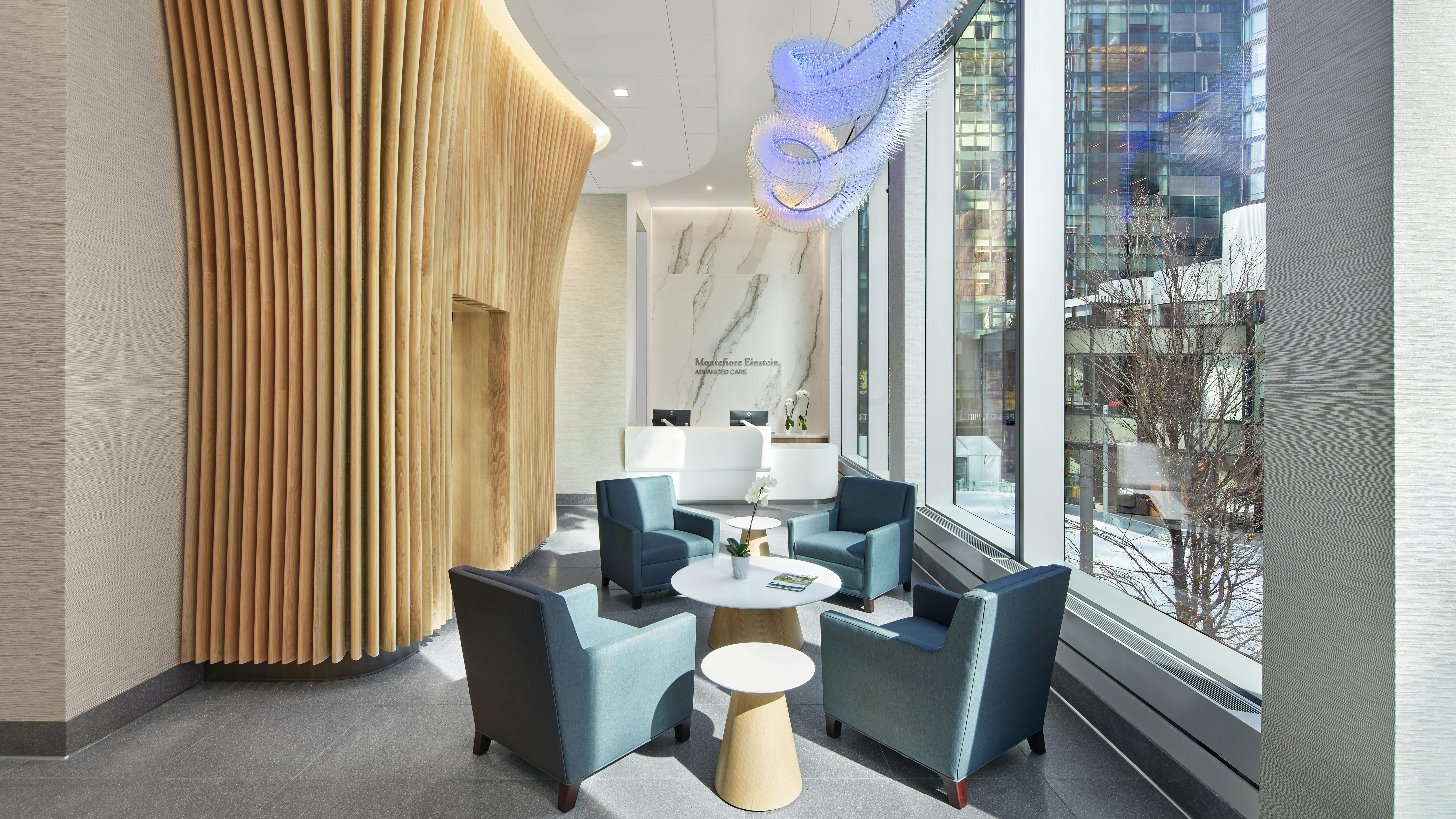 FCA Montefiore Manhattan West Entrance for healthcare facility with wood composite wall feature, bespoke light sculpture, natural daylight, and comfortable seating arrangement.