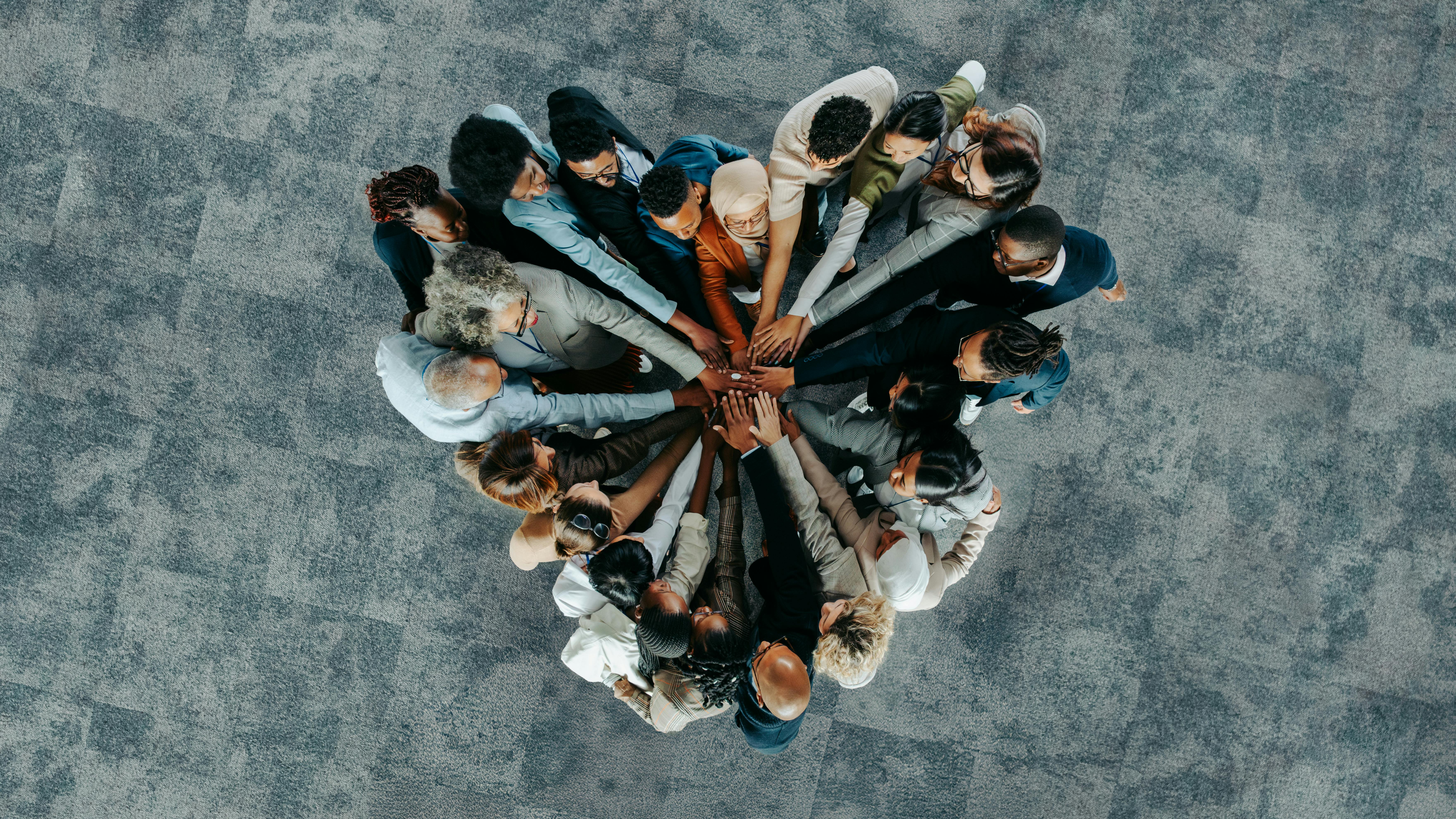 Overhead view of a team of people with their hands joined in center forming the shape of a heart.