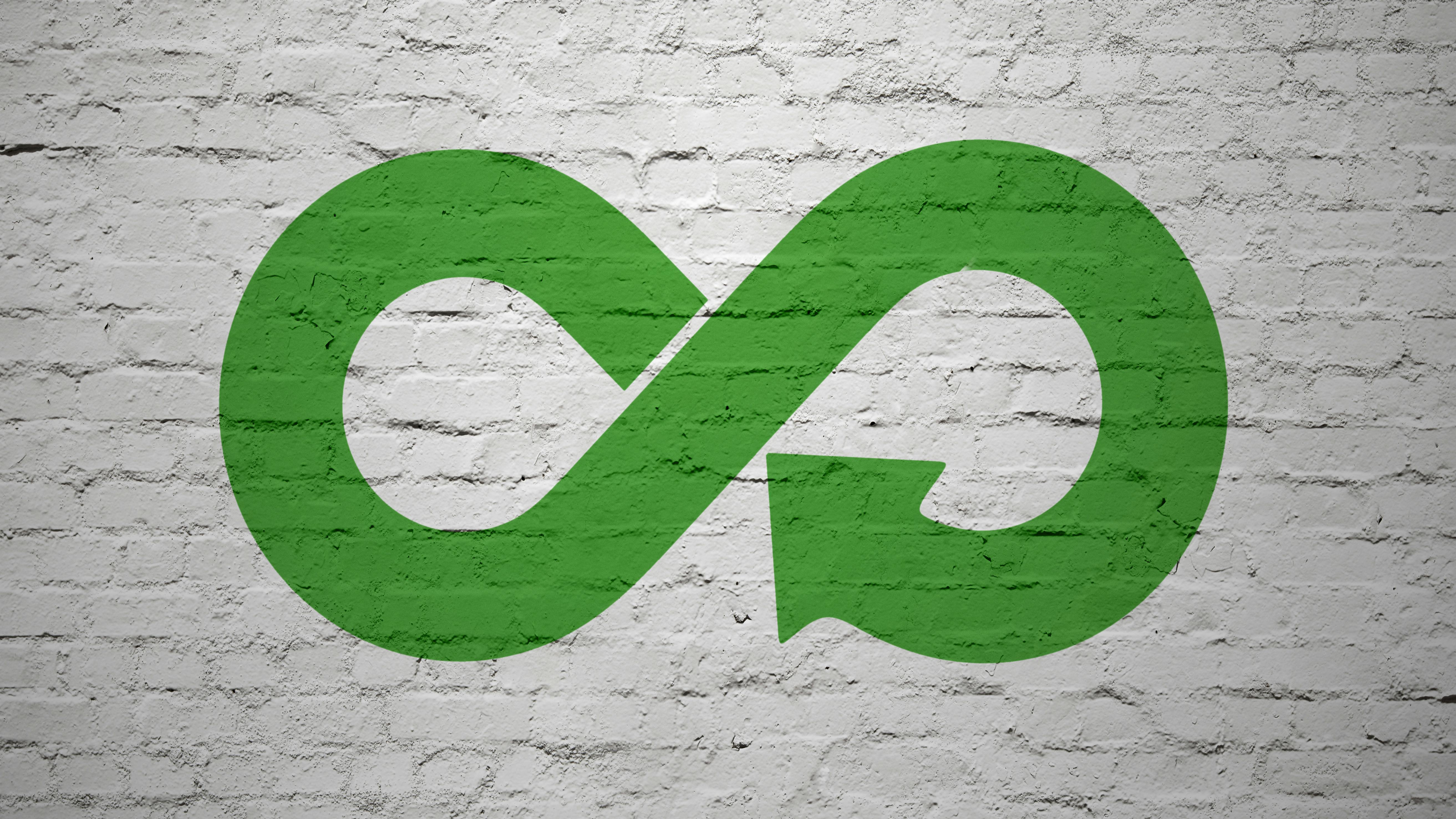 Green infinity symbol with recycling arrows overlaid against white brick wall.
