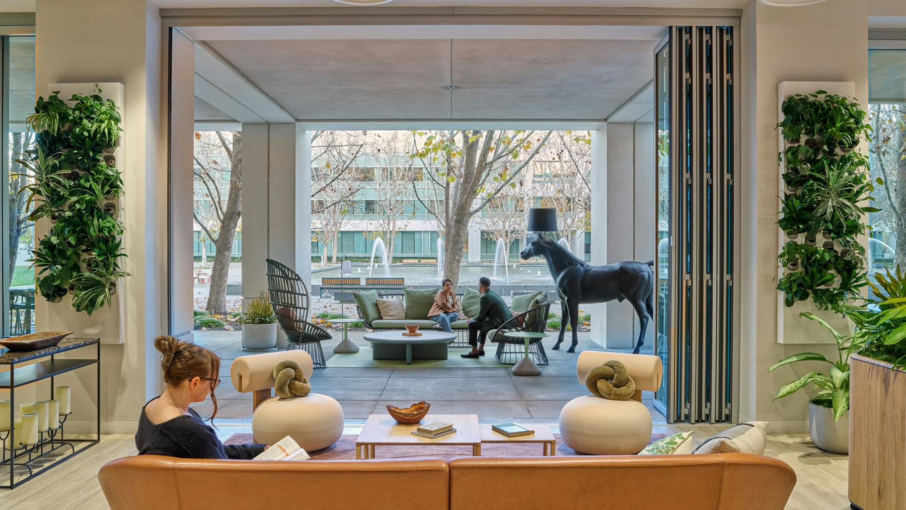 Interior view of a comfortable lounge with greenery and soft furnishings opening directly to an outdoor patio, bringing in natural light and views.