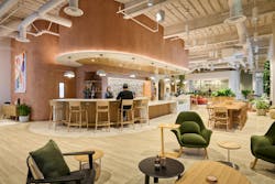 Curved café bar in a spacious open floorplan with soft neutral walls, light-toned flooring, comfortable lounge seating, and mixed pendant lighting creating a hospitality ambiance. Curved café bar in a spacious open floorplan with soft neutral walls, light-toned flooring, comfortable lounge seating, and mixed pendant lighting creating a hospitality ambiance.