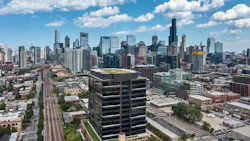 Daytime exterior view of the Fulton Labs building at 400 N Aberdeen in Chicago’s Fulton Market district, showing its glass curtainwall facade, dark metal mullions, adjacent city skyline, and urban street frontage.