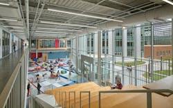 View from top of wood staircase overlooking two-story atrium space with public seating and glass wall in background. View from top of wood staircase overlooking two-story atrium space with public seating and glass wall in background.