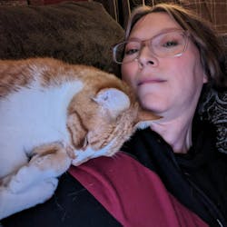Carrie Meadows reclines on a couch with an orange and white tabby cat Carrie Meadows reclines on a couch with an orange and white tabby cat