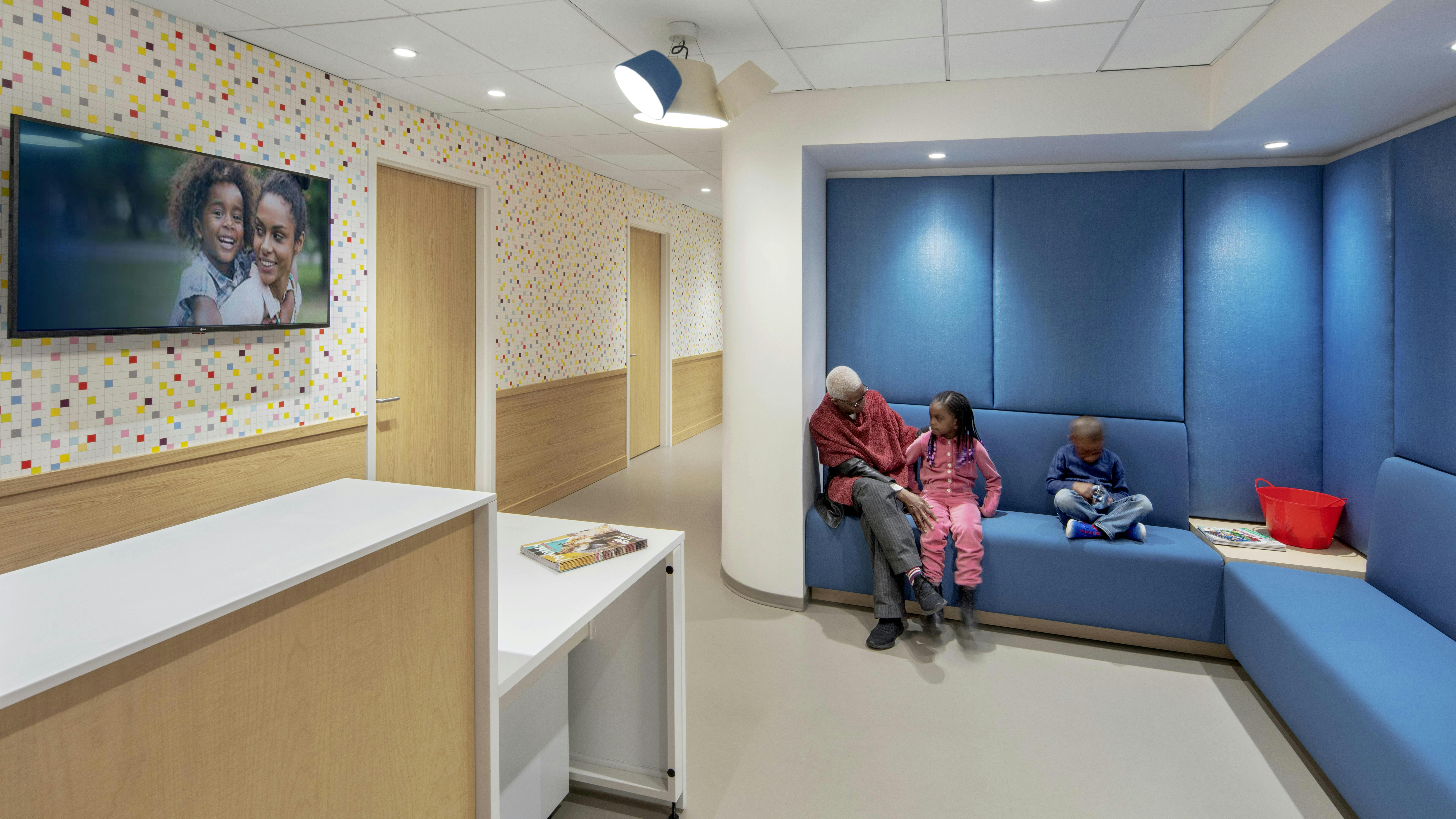 SCO Family of Services Genovese Family Life Center featuring blue upholstered seating area with patients waiting near long counter.