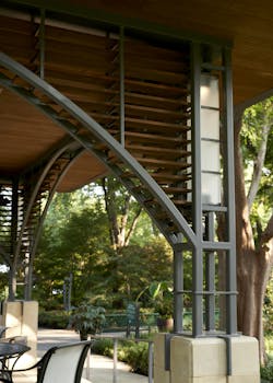 Close up of arboretum pavilion steel frame and archway, with rich, warm-toned slatted wood louvers and closed ceiling. Close up of arboretum pavilion steel frame and archway, with rich, warm-toned slatted wood louvers and closed ceiling.