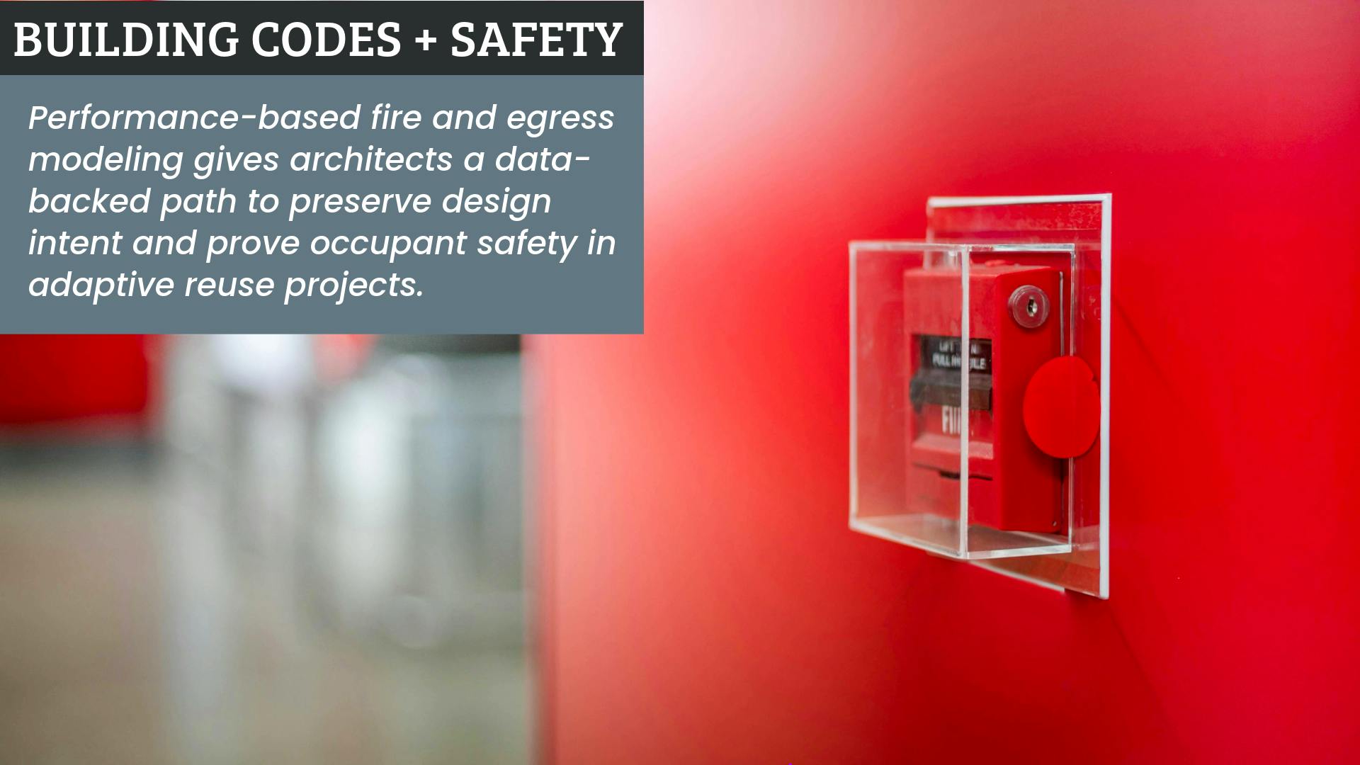 Wall-mounted fire alarm encased in plexiglass with blurred background.