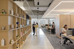 A view of the flexible work zones shows products on neutral wood shelving and adjoining workstations. A view of the flexible work zones shows products on neutral wood shelving and adjoining workstations.