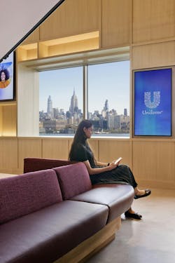 Woman sits on a curved, burgundy-upholstered bench seat, next to deep-set windows that show the Manhattan skyline. Woman sits on a curved, burgundy-upholstered bench seat, next to deep-set windows that show the Manhattan skyline.