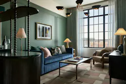 Guest suite at Fidelity Hotel featuring plush furniture, coffee table, lamps, and dark green accent wall next to windows. Guest suite at Fidelity Hotel featuring plush furniture, coffee table, lamps, and dark green accent wall next to windows.