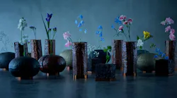 A variety of dark-colored vases with flowers against a blue background. A variety of dark-colored vases with flowers against a blue background.