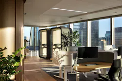 Light-filled office with desks in foreground and privacy pods in background against floor-to-ceiling windows. Light-filled office with desks in foreground and privacy pods in background against floor-to-ceiling windows.