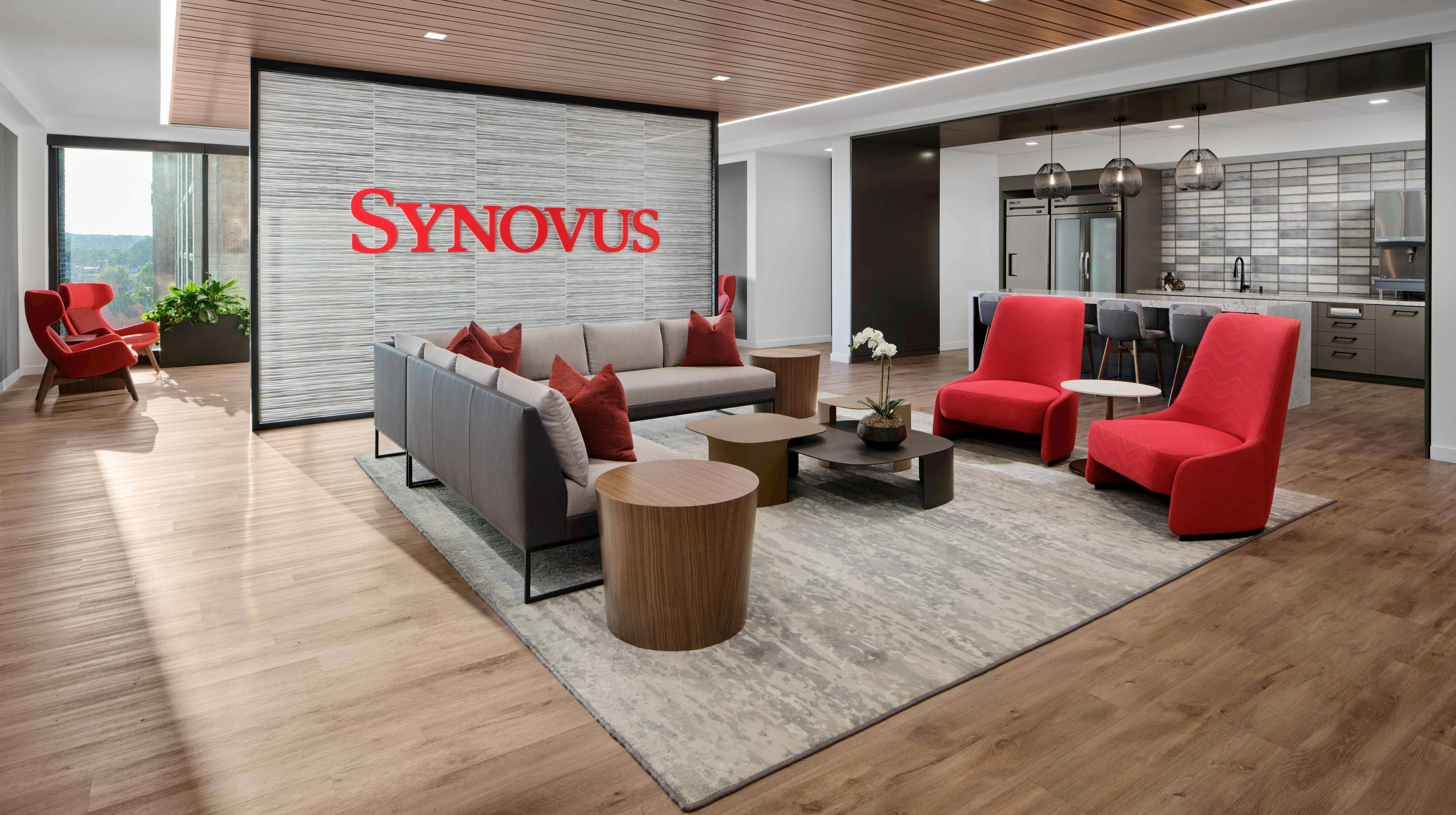 Open cafe and lounge area with Synovus red branding and accents grounded by neutral wood and stone look surfaces