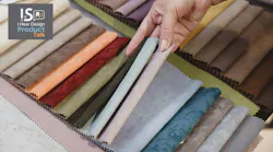 A hand holds swatches of textiles set on a table.