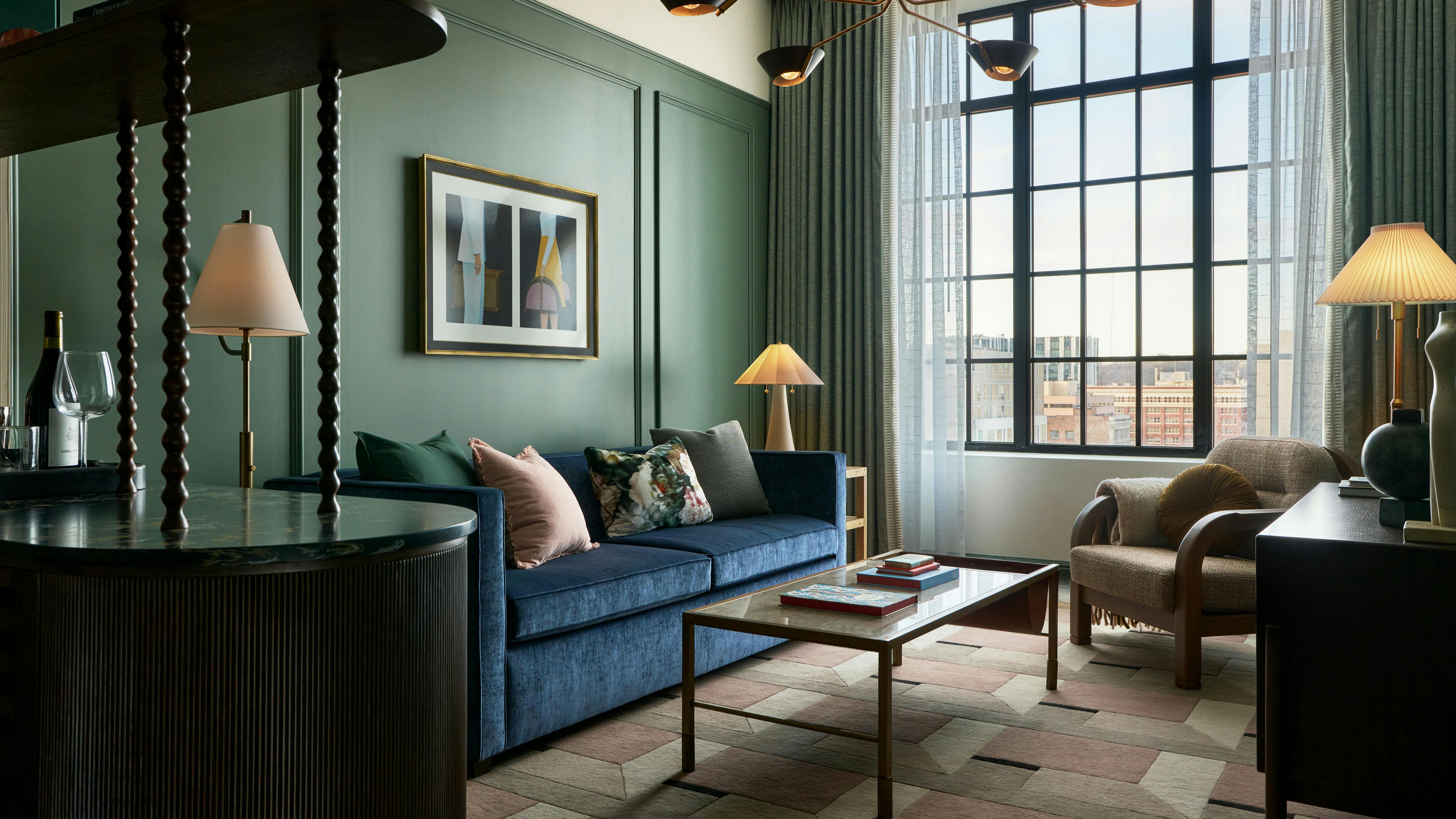 Chic hotel room with emerald green walls, plush blue sofa, and neutral geometric pattern carpeting