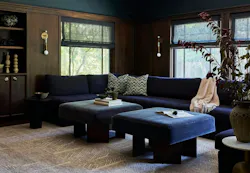 Wood-paneled residential living area with navy blue commercial-grade upholstered sectional sofa, modern wall sconces, and patterned neutral carpet tile. Wood-paneled residential living area with navy blue commercial-grade upholstered sectional sofa, modern wall sconces, and patterned neutral carpet tile.