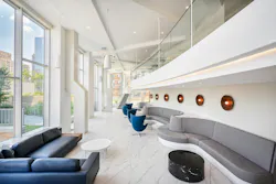 Expansive co-working lounge with crisp white surfaces, layered lighting, bench and individual ergonomic seating, and wide window views/access to outdoor spaces. Expansive co-working lounge with crisp white surfaces, layered lighting, bench and individual ergonomic seating, and wide window views/access to outdoor spaces.