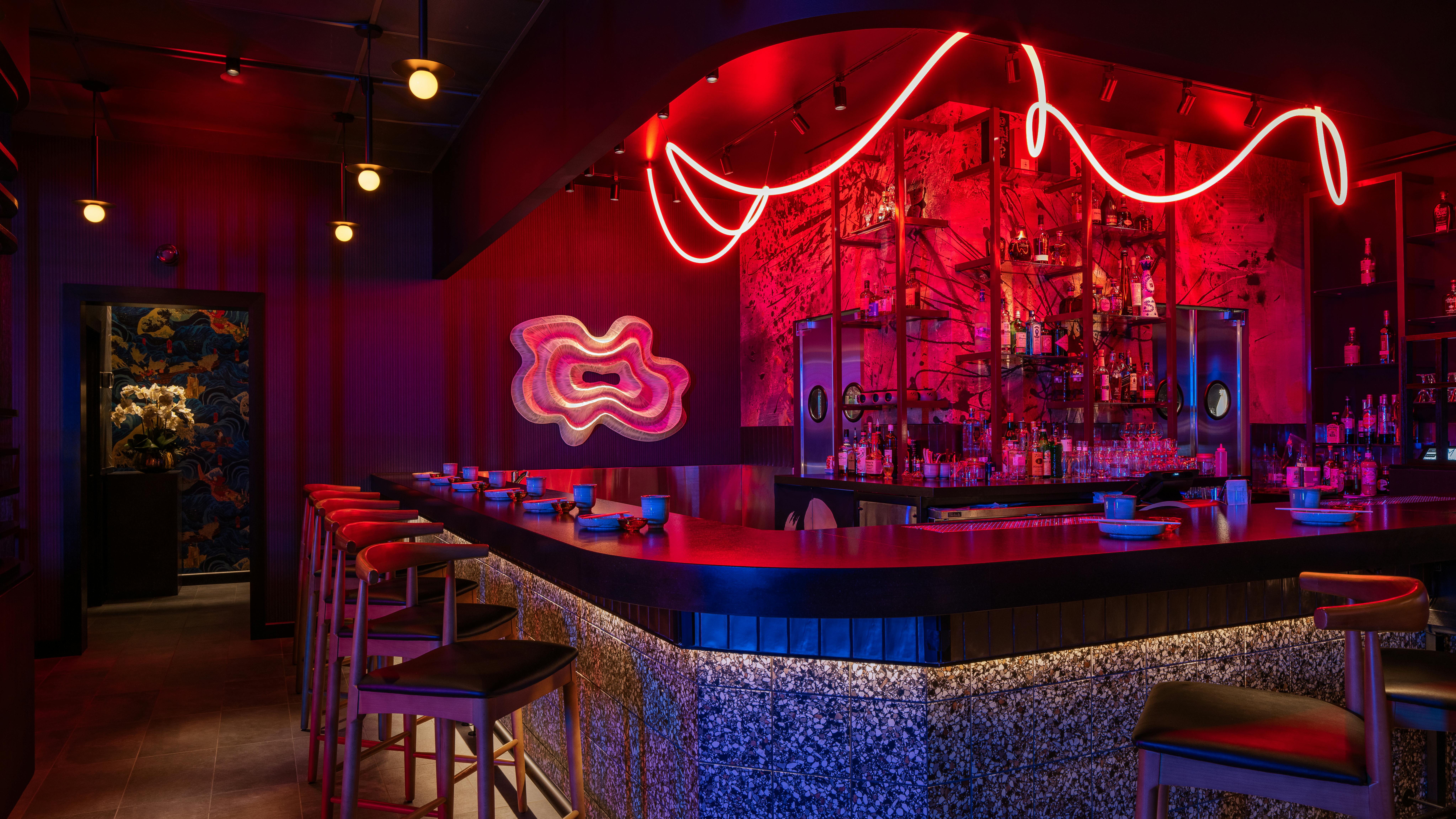 Naisho Room bar with looping, draped LED lighting overhead, integrated color-changing cove and under-counter lighting, sleek stone-look surfaces, and a dark, moody color palette
