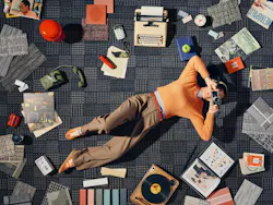 Woman holding a vintage camera lying down on geometric grid-patterned carpet tiled floor with flooring samples scattered around Woman holding a vintage camera lying down on geometric grid-patterned carpet tiled floor with flooring samples scattered around