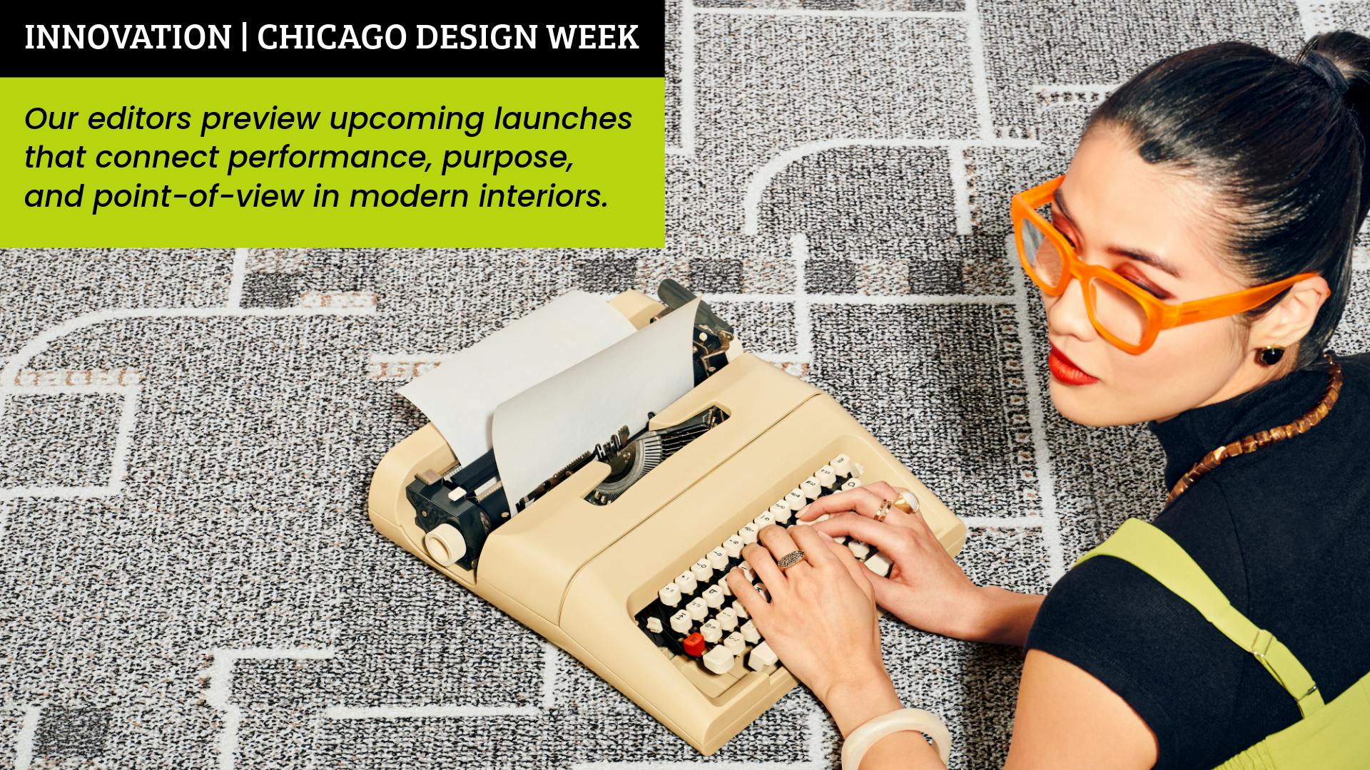 Woman wearing orange framed glasses lays on her stomach on patterned carpeting, while working on a vintage typewriter