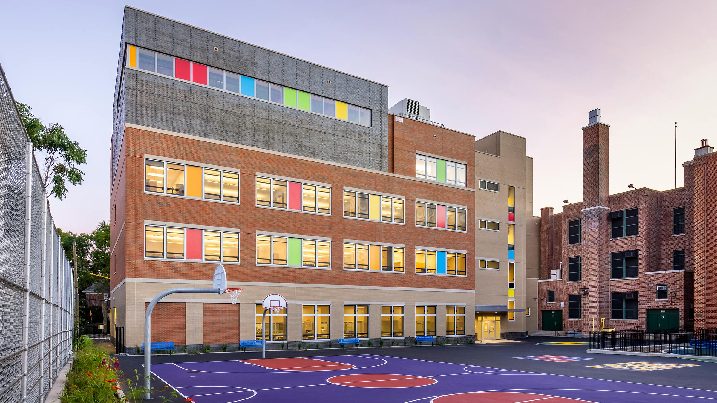 Exterior of colorful K-12 building in background with basketball court in foreground.