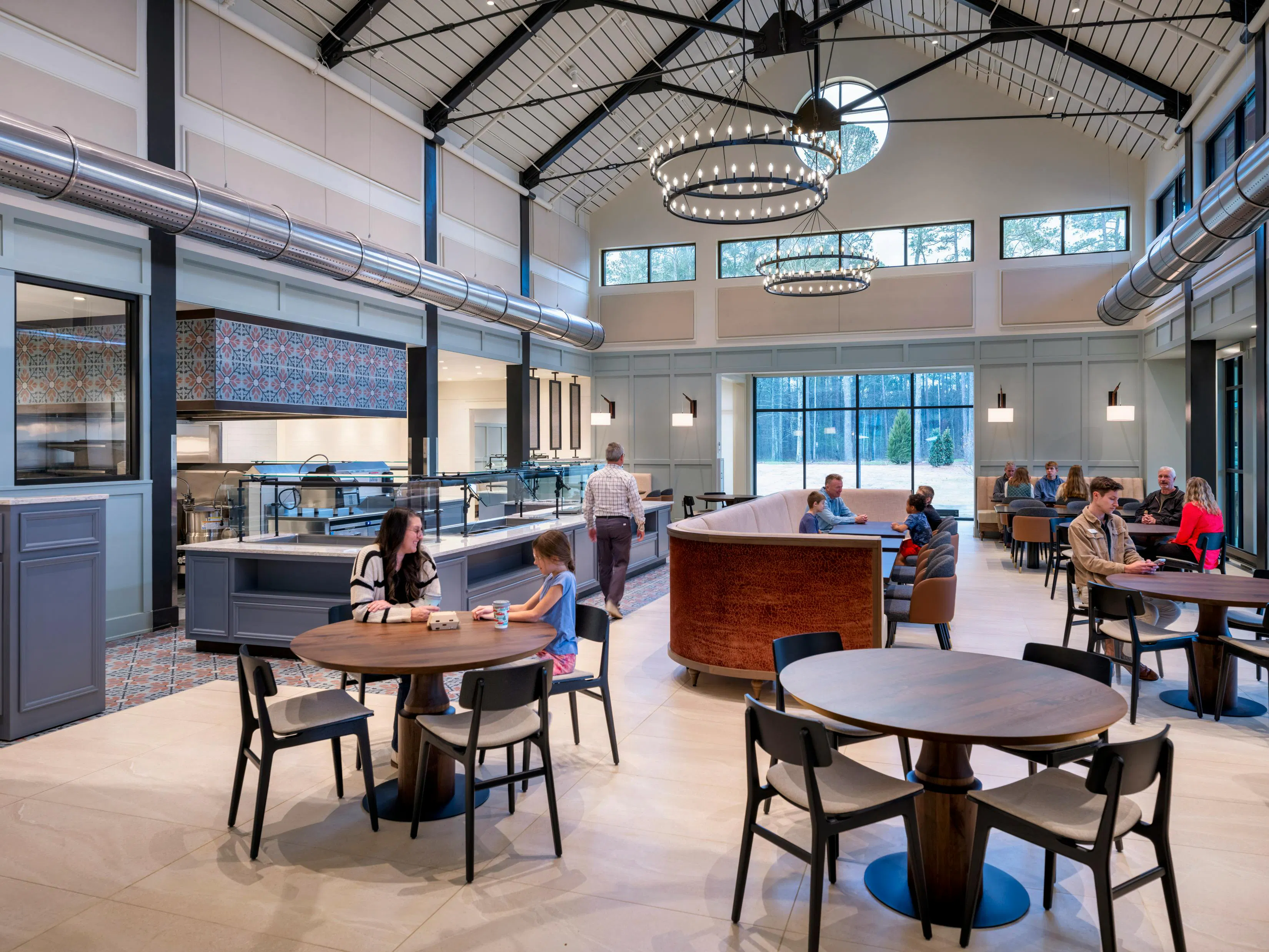 Amber Grace Community dining facility with open ceiling, circular chandelier lighting, restaurant style booths, and round tables with chairs. Amber Grace Community dining facility with open ceiling, circular chandelier lighting, restaurant style booths, and round tables with chairs.