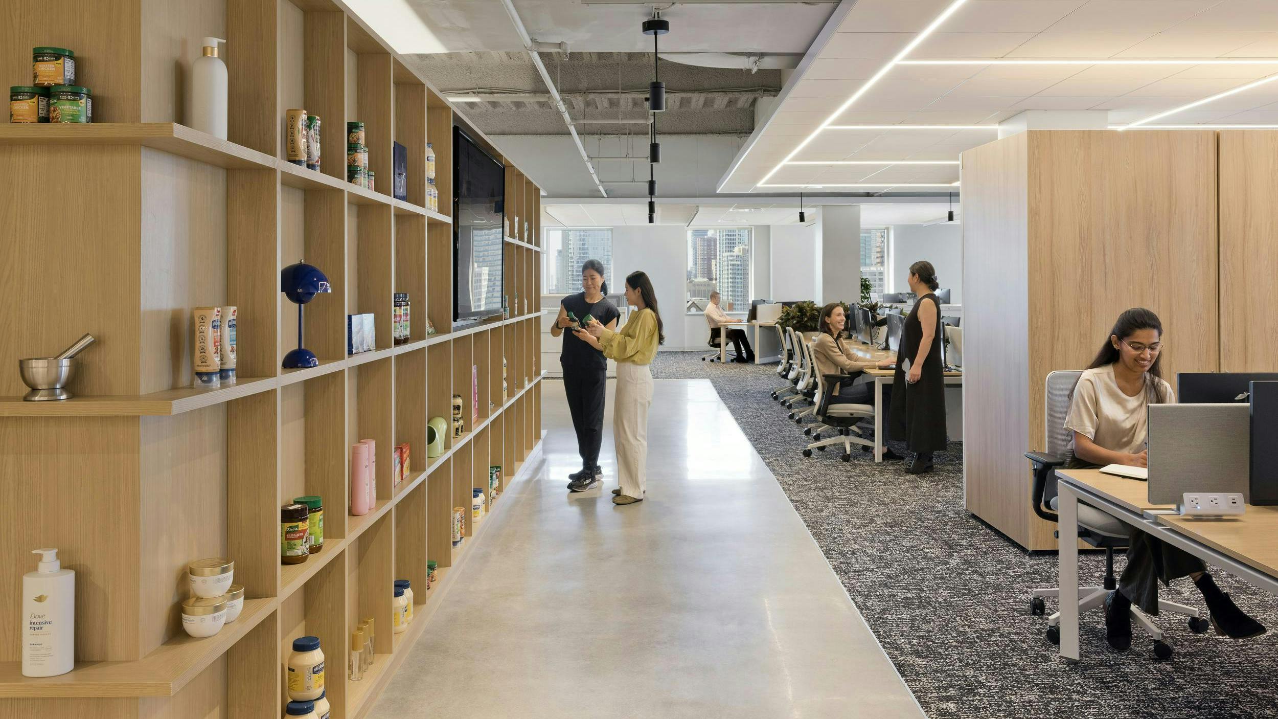 A view of the flexible work zones shows products on neutral wood shelving and adjoining workstations.