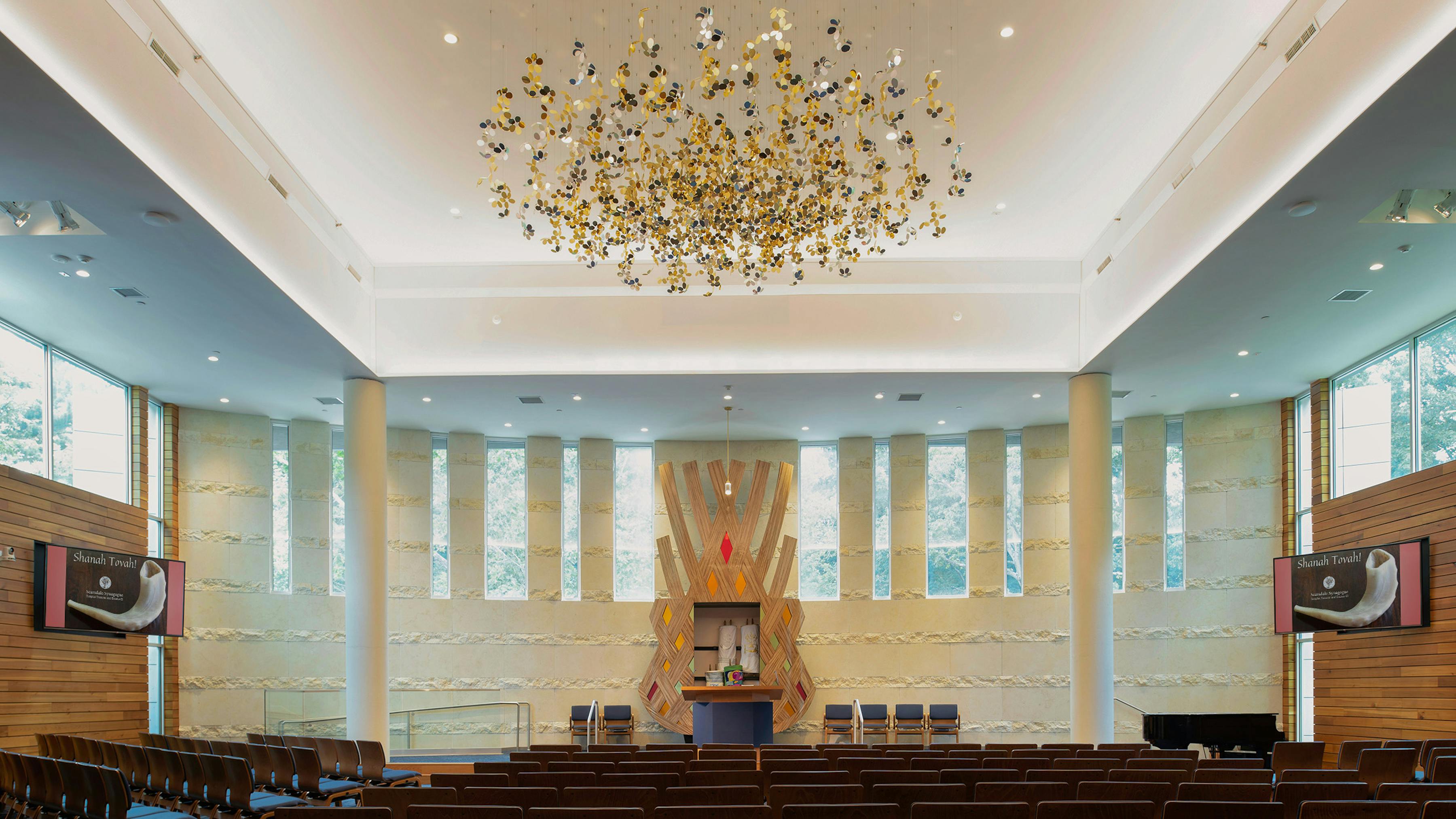 Contemporary synagogue space with clerestory windows and sculptural element overhead facing altar.
