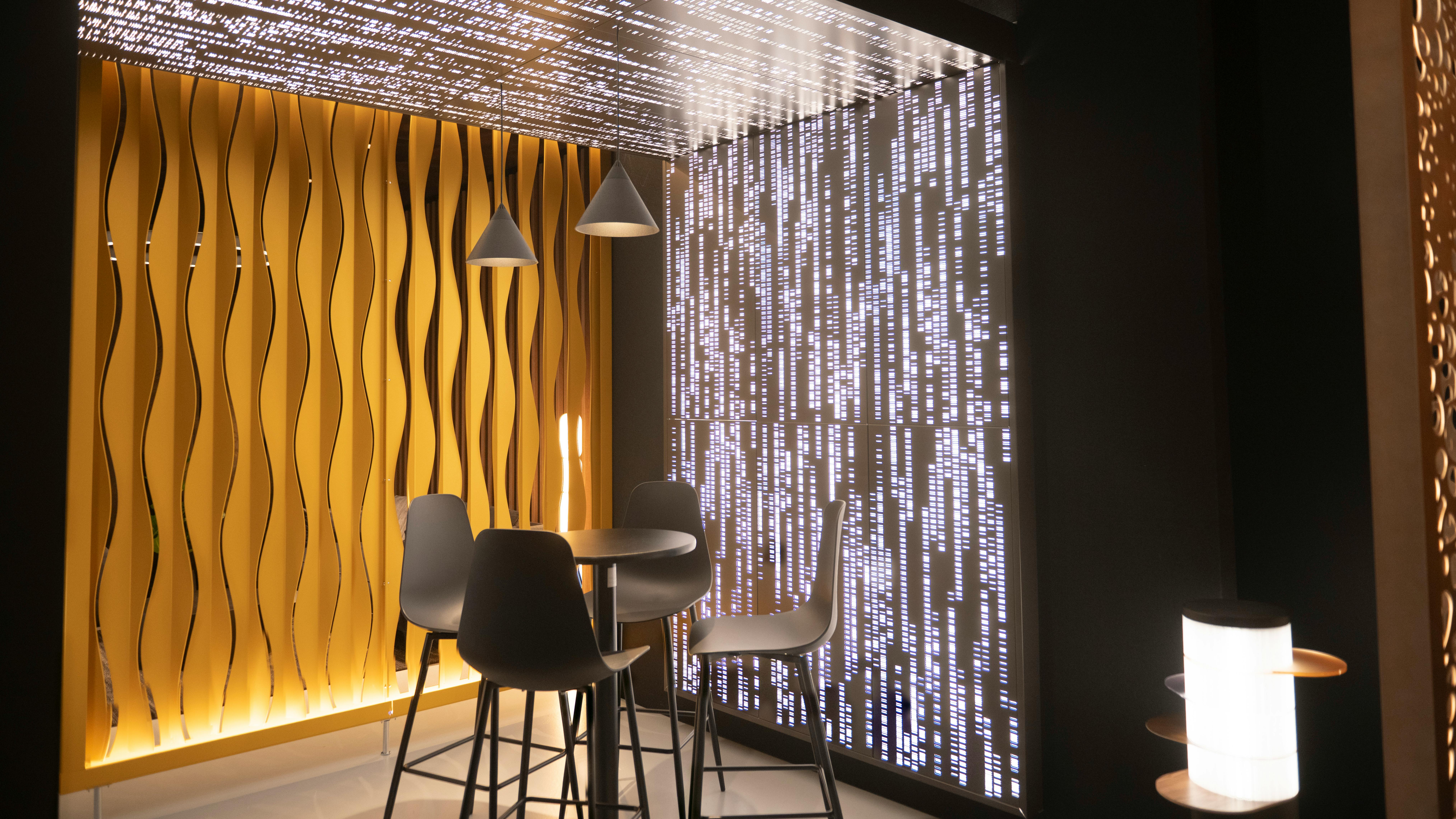 AWI showroom zone 7 with cafe style vignette, showing Particle Code backlit feature wall, decorative wall surface, and LightArt pendants
