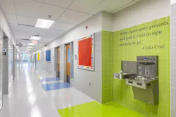 Interior public school corridor grounded in lighter neutrals, with a section of lime green tilework on the wall featuring a quote from Celia Cruz