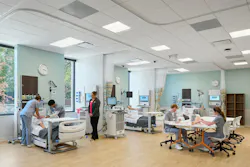 A simulation classroom shows nursing students practicing on manikins on hospital beds while other students collaborate at a shared workstation