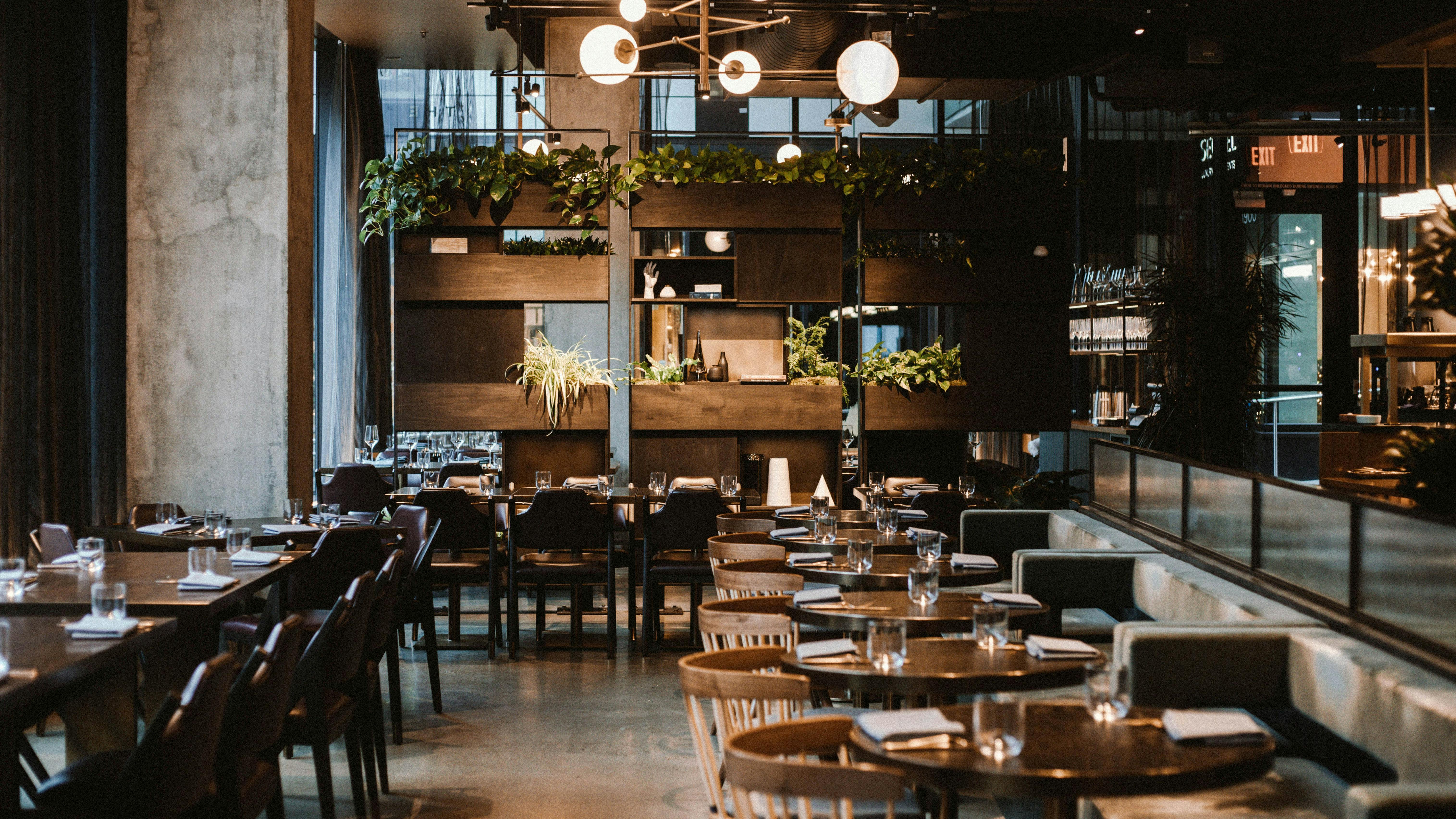 Interior design of restaurant in an upmarket hotel uses stone-look finishes, mixed dark upholstery and light wood furnishings, and unique pendant lighting